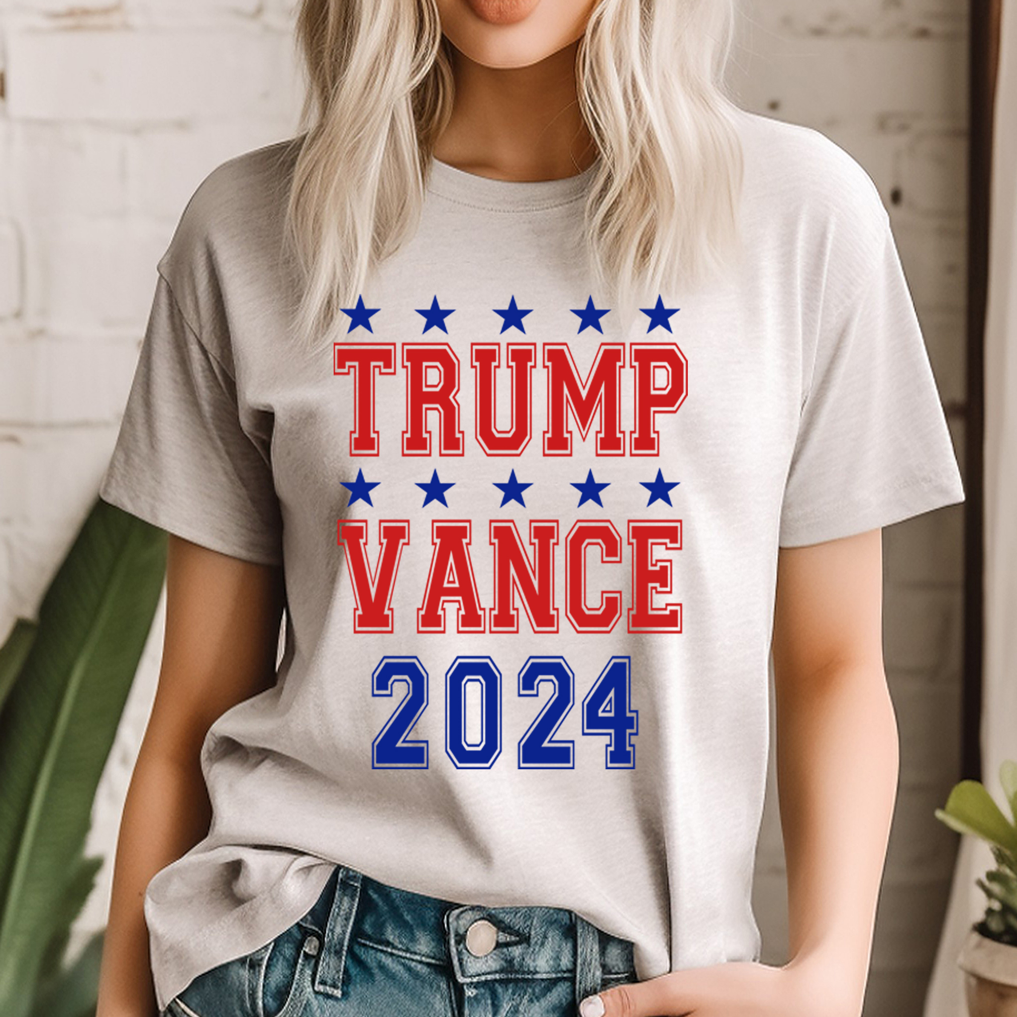 A model wearing a tan crew neck t-shirt with stars ad 2024 in blue and the words TRUMP VANCE in red